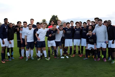 Un grupo de estudiantes del Abbey College en Cambridge está junto en un campo de fútbol bajo un cielo nublado.