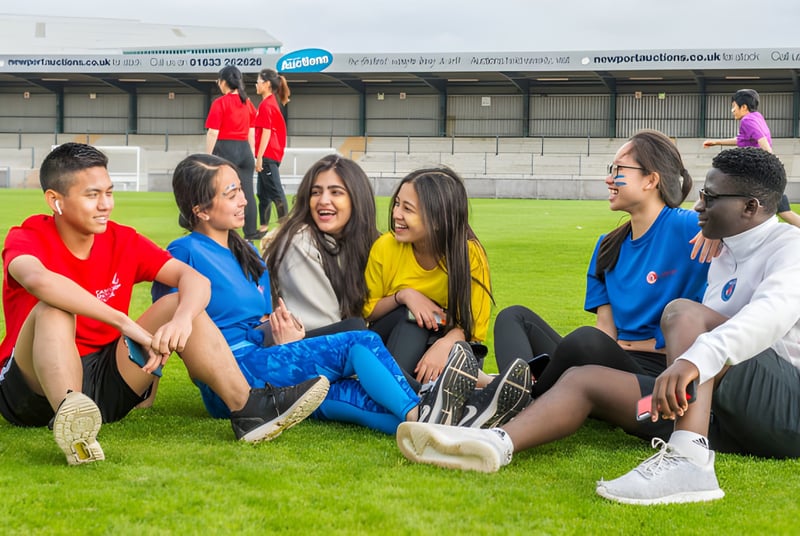 Un grupo de estudiantes se sienta en el campo frente a un edificio en el campus del Abbey College.