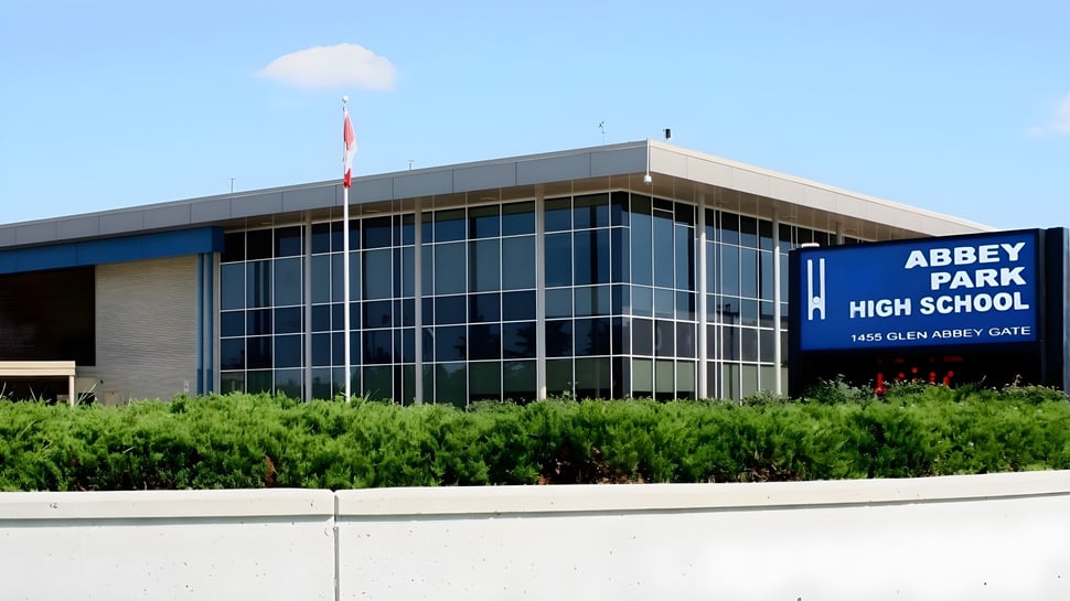 El moderno edificio escolar de la Abbey Park High School con fachada de vidrio está rodeado de vegetación verde.