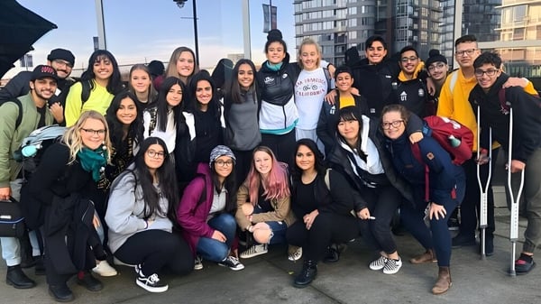 Un grupo de alumnas está frente a altos edificios y un cielo nublado en el campus de la Abbotsford Senior Secondary School.