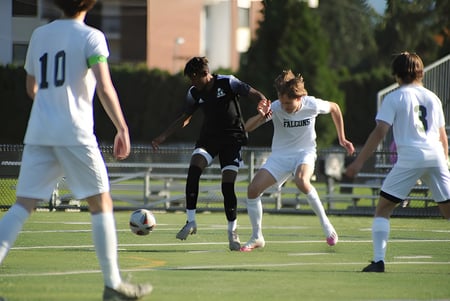 Un grupo de estudiantes juega al fútbol en el campo verde de la Abbotsford Senior Secondary School con edificios y árboles de fondo.