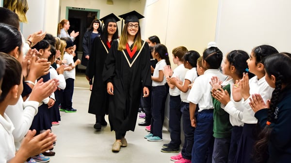 Los graduados de la Abbotsford Traditional Secondary School caminan en sus togas a través de un pasillo lleno de estudiantes que vitorean.
