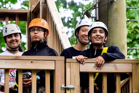 Estudiantes de la Abbotsford Traditional Secondary School están con cascos y ropa de seguridad en una plataforma de madera en el campo.