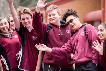 Un grupo de estudiantes de la Aberfoyle Park High School está junto a una pared de ladrillo rojo al aire libre.