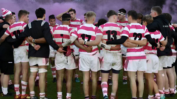 Un grupo de jugadores de rugby en camiseta a rayas rosa y blanca está en un huddle en el campo de la Abingdon School.