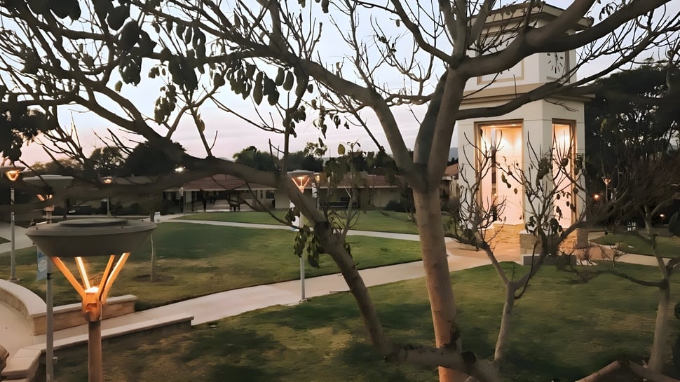 El área exterior con terraza y césped verde en el campus de la Academy MiraCosta está rodeada de edificios y árboles desnudos.