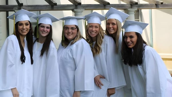 Un grupo de jóvenes mujeres en vestidos de graduación blancos está de pie en el edificio escolar de la Academy of Notre Dame.