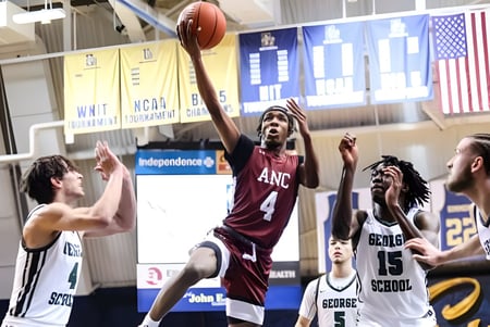 Partido de baloncesto con jugadores de la Academy of the New Church en un gimnasio con banderas estadounidenses.