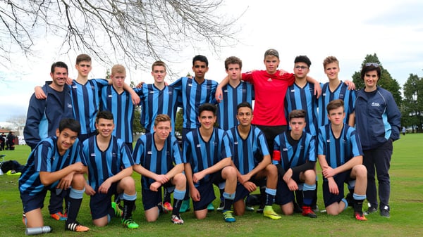 Un grupo de jóvenes futbolistas de ACG Strathallan está reunido en un campo de césped con árboles desnudos al fondo.