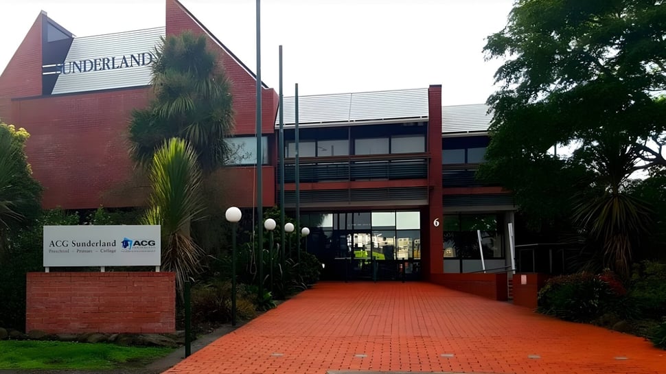 El edificio de ladrillo con fachada roja en el campus de la ACG Sunderland está rodeado de plantas verdes.