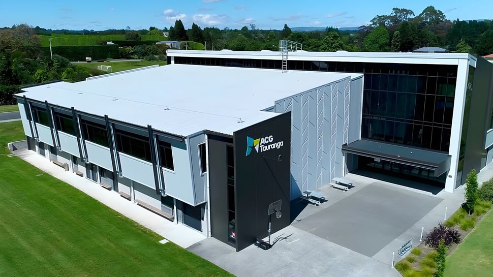 El moderno edificio de varios pisos de ACG Tauranga se encuentra en un paisaje verde con grandes ventanas.