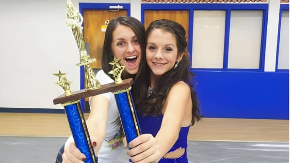 Dos estudiantes de la Acorn High School sostienen sonriendo un trofeo en una sala con paredes azules.