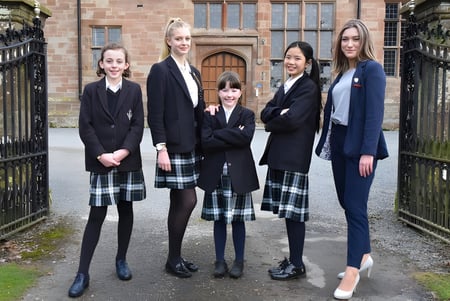 Un grupo de estudiantes de la Adcote School está frente a un edificio de ladrillo con puertas decoradas.