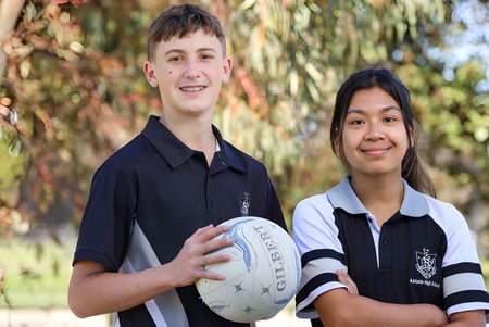 Dos estudiantes de la Adelaide High School están juntos al aire libre sosteniendo un balón de rugby frente a unos árboles.