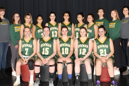 Un grupo de jóvenes jugadoras de baloncesto en camisetas verdes y amarillas posan frente a una cortina negra en el campus del Aden Bowman Collegiate.