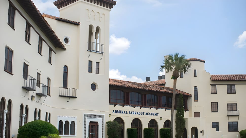 El edificio de la Admiral Farragut Academy muestra un estilo arquitectónico español con una alta torre y ventanas de arco frente a un cielo azul.