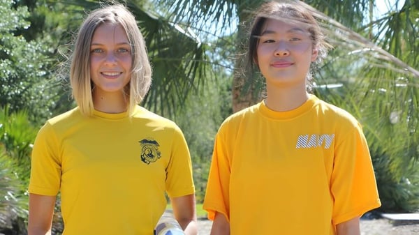 Dos estudiantes de la Admiral Farragut Academy están con camisas amarillas brillantes frente a palmeras en un entorno tropical.