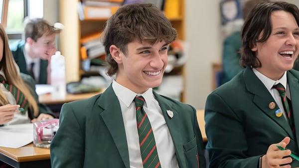 Dos estudiantes de la Akeley Wood School conversan y ríen en el aula con materiales escolares de fondo.
