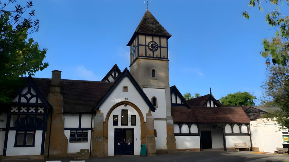 El edificio Tudor de la Akeley Wood School está rodeado de verde bajo un cielo azul claro.
