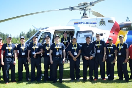 Un grupo de policías está frente a un helicóptero policial en un campo de hierba en el terreno de la Alberni District Secondary School.