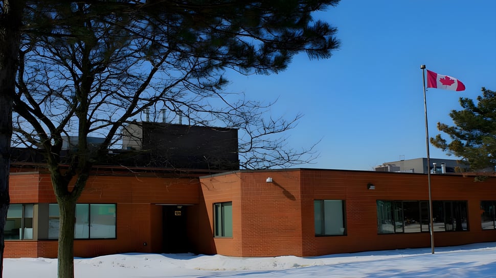 El edificio de ladrillo del Albert Campbell Collegiate Institute en un día nevado con la bandera canadiense y árboles de fondo.