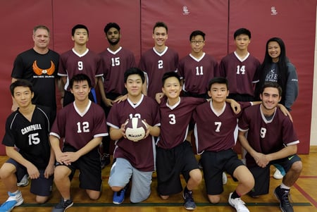 El equipo de voleibol del Albert Campbell Collegiate Institute posando juntos en el gimnasio frente a una pared roja.