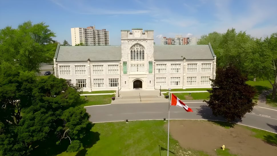 El edificio histórico del Albert College se encuentra en un cuidado jardín con árboles y rascacielos al fondo.