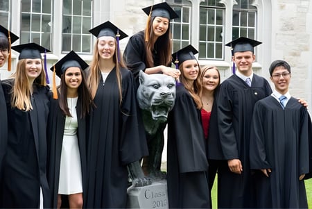 Un grupo de graduadas y graduados, así como un perro, posan frente a un edificio en el campus del Albert College.