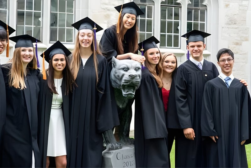 Un grupo de graduadas y graduados, así como un perro, posan frente a un edificio en el campus del Albert College.