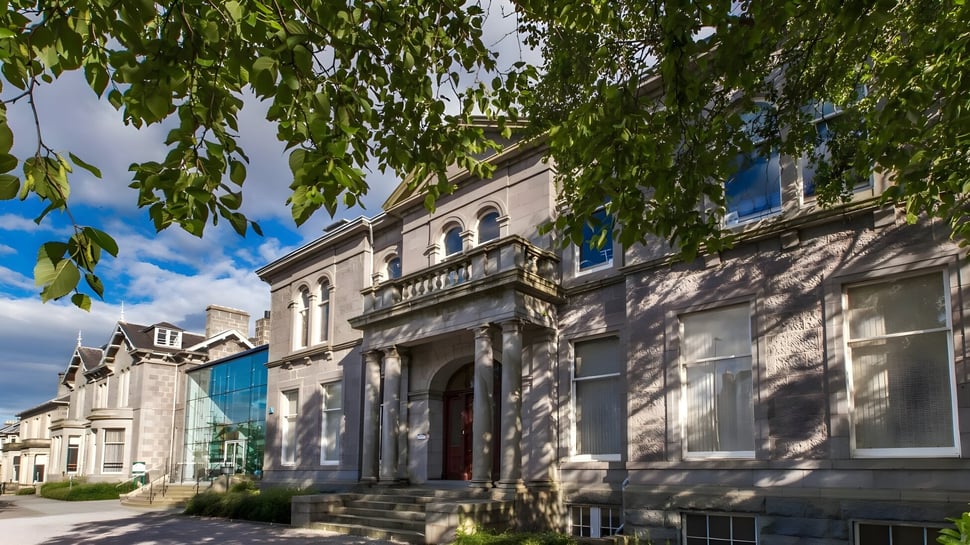 El histórico edificio de varios pisos con arquitectura decorada se encuentra en el terreno de la Albyn School y está rodeado de vegetación verde.