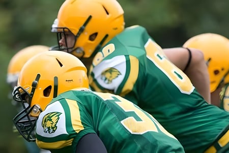 Un grupo de jugadores de fútbol americano de la Aldershot High School está en el campo de fútbol con camisetas verdes y amarillas.