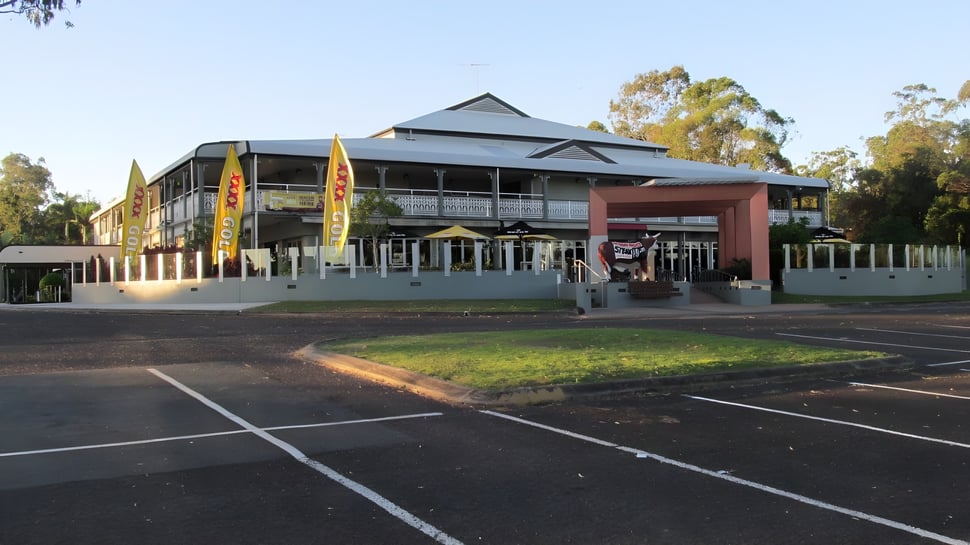 El moderno edificio de varios pisos de la Alexandra Hills State High School se encuentra en un entorno verde con árboles y estacionamientos en primer plano.