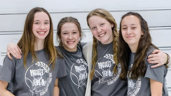 Cuatro estudiantes de la Algoma Christian High School están juntos frente a un fondo neutro y sonríen.