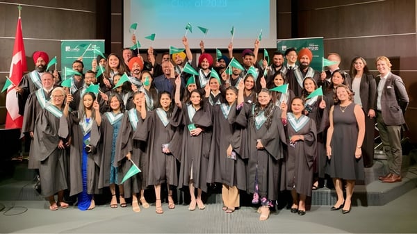 Un gran grupo de graduadas y graduados está frente a un logo de Algonquin College en sus togas de graduación.