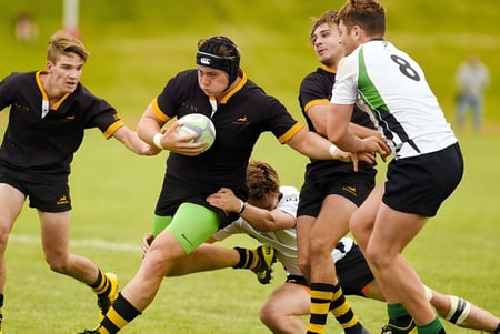 Estudiantes de la All Saints Anglican School juegan un intenso partido de rugby en un campo verde.