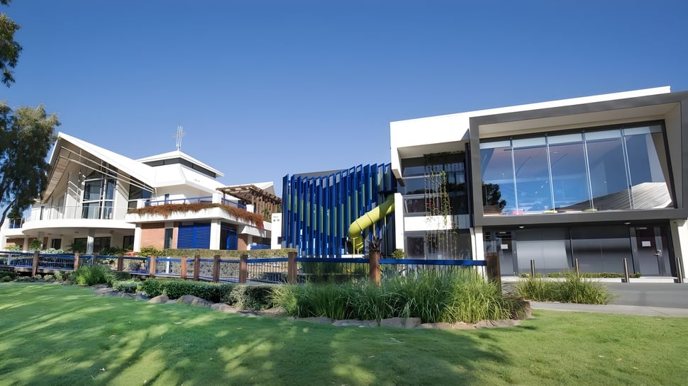 El moderno edificio de varios pisos de la All Saints Anglican School está rodeado de césped bien cuidado y plantas bajo un cielo azul claro.