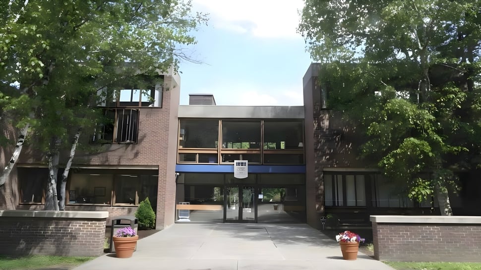 El moderno edificio de ladrillo de la Allendale Columbia School con grandes ventanas y entrada cubierta rodeada de árboles.