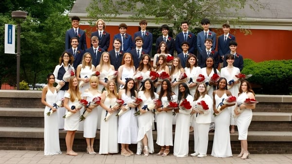 Un gran grupo de personas está en ropa formal frente a un edificio en la escalera del campus de la Allendale Columbia School.