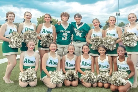 Un grupo de animadoras posando en uniformes verdes y blancos en el campo deportivo de la Alma High School.