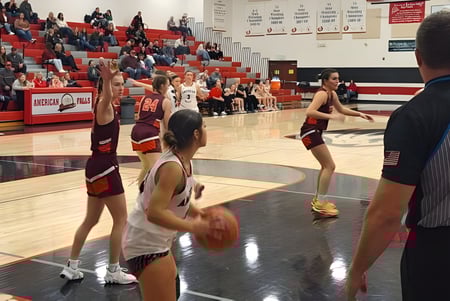Estudiantes de la American Falls High School juegan un partido de baloncesto en el patio de la escuela con espectadores en las gradas.