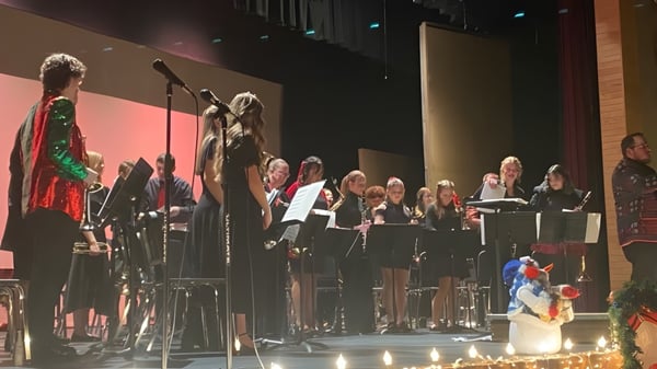 El coro y los músicos de la American Falls High School se presentan en un escenario frente a un público en una sala oscurecida.