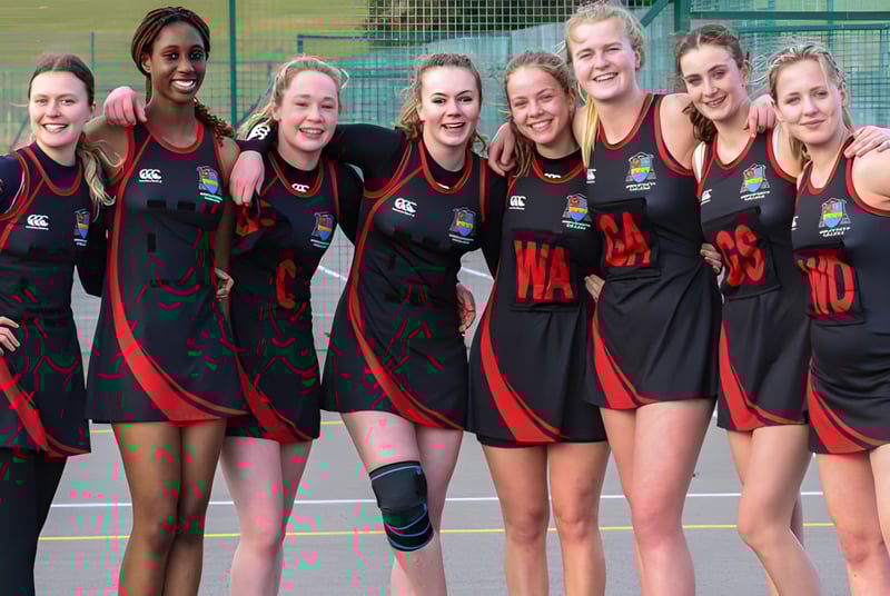 Un equipo de atletas en uniformes negros y rojos posan juntos en el campo deportivo del Ampleforth College.