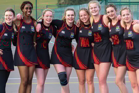 Un grupo de deportistas femeninas posan juntas en el campo de deportes del Ampleforth College frente a una cerca.