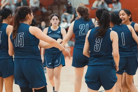Un grupo de jóvenes jugadoras de baloncesto en camisetas azul oscuro están en el campo de baloncesto del Anaheim Union High School District.