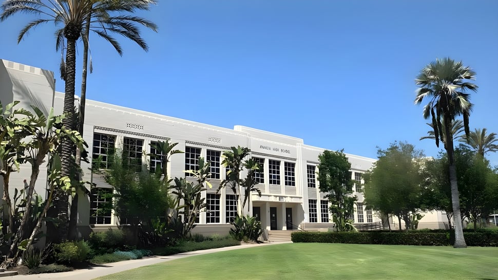 El edificio blanco de varios pisos con ventanas de arco del Anaheim Union High School District frente a palmeras y un cielo azul.