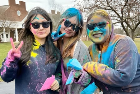 Tres estudiantes de la Andrews Osborne Academy están en ropa colorida y gafas de sol frente a una casa en el campo.