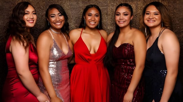 Cinco estudiantes del Aorere College posan en vestidos de gala frente a un fondo cálido y texturizado.