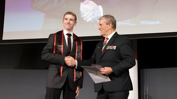 Dos hombres en traje formal se dan la mano en el escenario frente a una pantalla de proyección en el campus de la Applecross Senior High School.