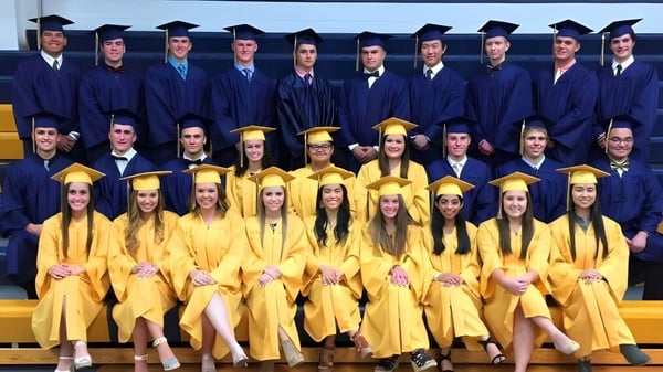 Graduados y graduadas de Aquin High School en togas azules y amarillas frente a un fondo amarillo.