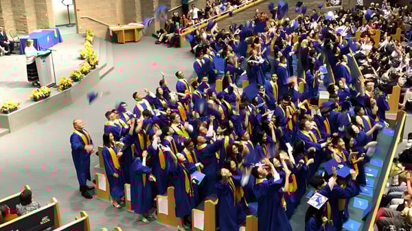Un gran grupo de graduadas y graduados en togas azules y doradas se reúne en el auditorio de la A.R. MacNeill Secondary School durante una ceremonia de graduación.